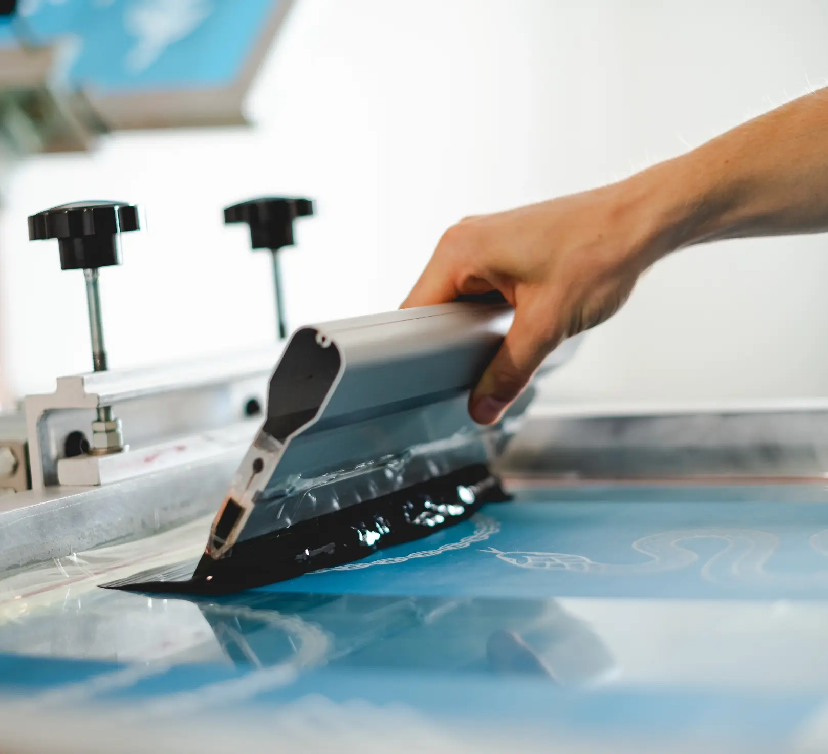 Pulling water-based ink across a screen on press at Alpine Apparel Co