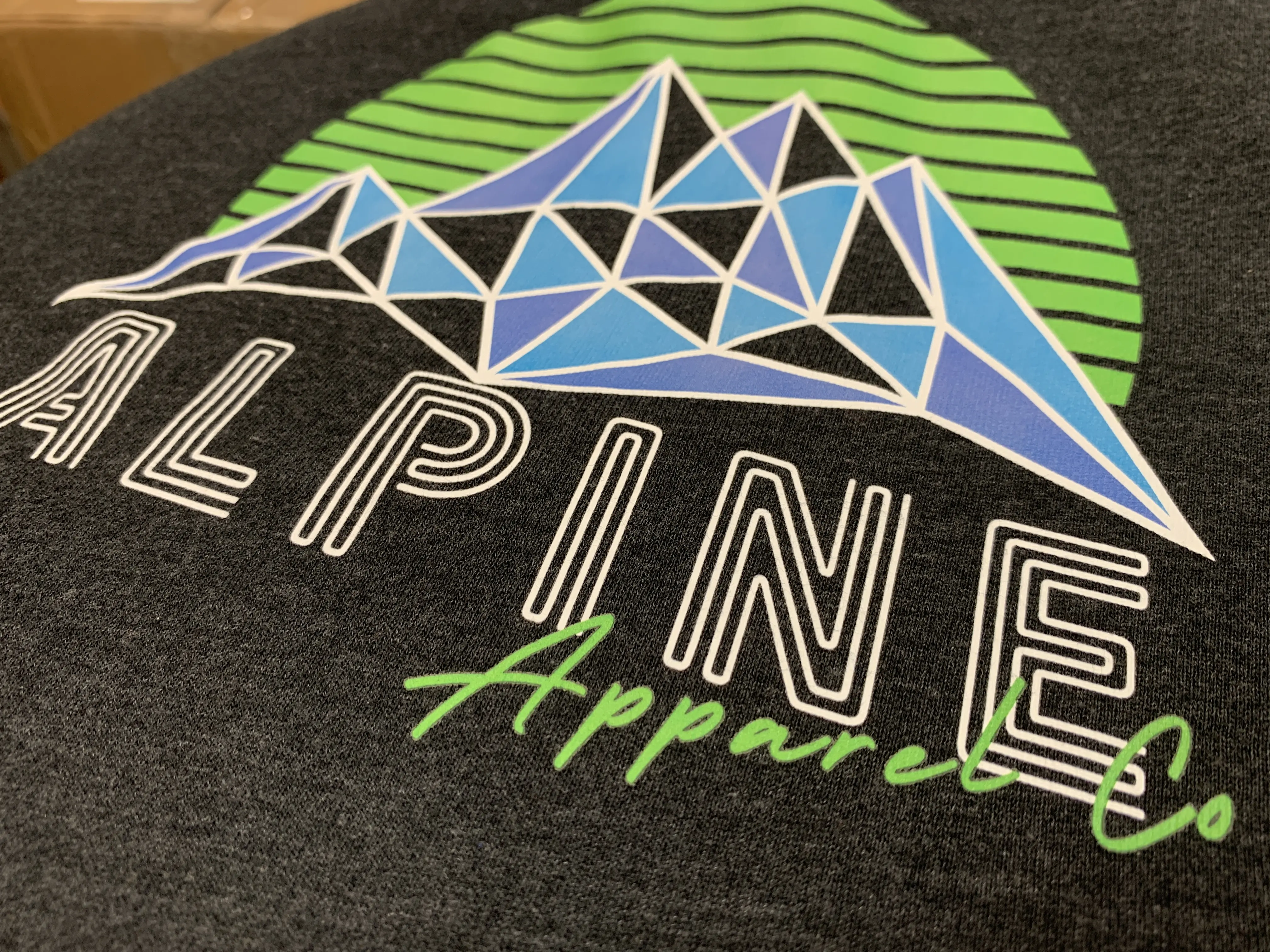 Multi-color water-based screen print of a geometric mountain on a charcoal hoodie, printed by Alpine Apparel Co in Castle Rock, Colorado